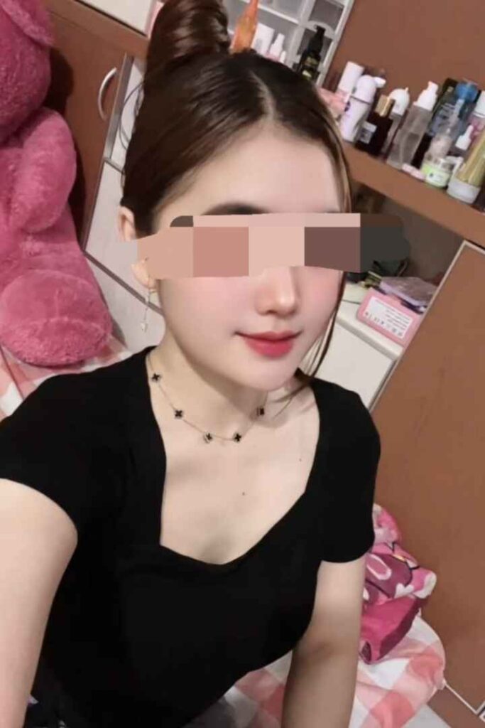 Young woman with hair in a bun, wearing a black top and clover necklace.